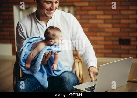 man working at desk at home with laptop, holding cute babys, looking at screen