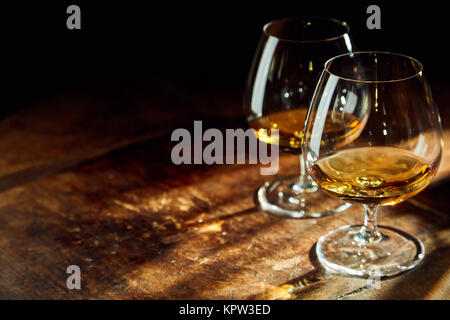 Close up of two bourbon filled glasses on wooden table in a dark room with a few rays of sunlight Stock Photo