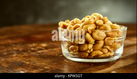 Glass bowl of fresh roasted salted peanuts or groundnuts on an old wooden table or bar counter in a side view with copy space Stock Photo
