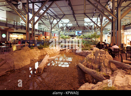 People in a waiting lounge of Vancouver International Airport, departures interior with restaurants and a beautiful resting area with an artificial po Stock Photo