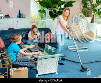 boy playing with computer, his sister using smartphone at home and mother doing homework Stock Photo