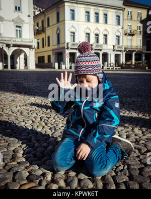 Beautiful little boy is sitting on the ground and shows that he is five years old in this sunny winter day. Happy Birthday Stock Photo