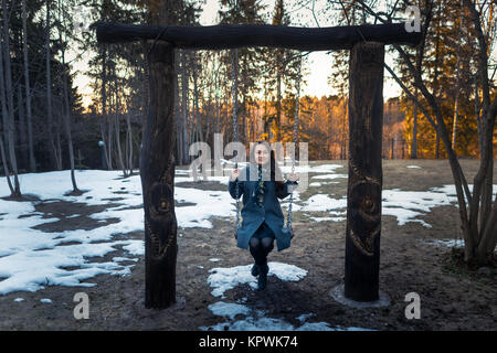 Happy young woman swinging on a swing have fun and smiling in the park in sunny winter day Stock Photo