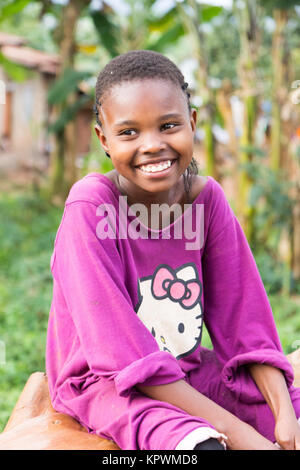 A beautiful laughing Ugandan girl sitting on a fallen tree trunk. Stock Photo