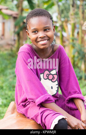 A beautiful laughing Ugandan girl sitting on a fallen tree trunk. Stock Photo