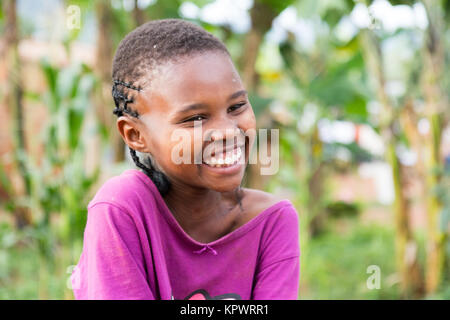 A beautiful laughing Ugandan girl sitting on a fallen tree trunk. Stock Photo