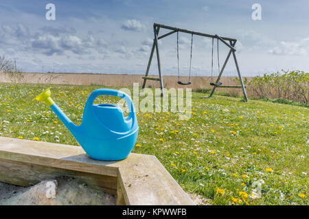 Kids watering pot on the edge of the sandbox with a swing in the background Stock Photo