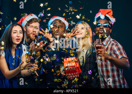 friends at New Year's party, wearing santa hats, dancing and blowing confetti Stock Photo