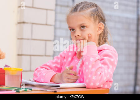 Schoolgirl thought drawing on the album in pencil, in the yard Stock Photo