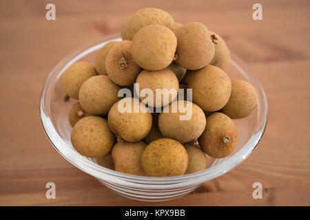 Bowl filled with an heap Dimocarpus Longan fruit isolated on wooden background Stock Photo