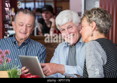 Three senior citizens using tablet computer in bistro Stock Photo