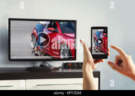 Closeup on woman hand holding smartphone and use a app with remote control. Focus on the remote control. transfer images from phone to TV screen using Stock Photo