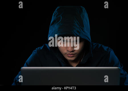Hacker in a dark hoody sitting in front of a notebook. Computer privacy attack Stock Photo