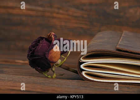 Notebook in leather cover and dried rose on wood Stock Photo