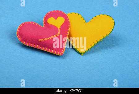 Two felt craft hearts, pink and yellow on blue Stock Photo