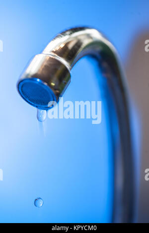 Water drips from the tap into a steel metal shell in blue tones close-up macro water runs out in the water supply shutdown liquid saving utility probl Stock Photo