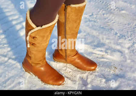 Leg woman winter brown fur boots walking on the snow in a winter park. Closeup outsole of warm boot. Stock Photo