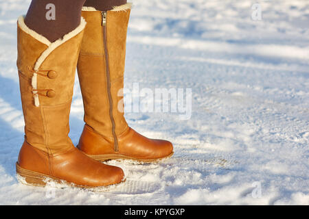 Leg woman winter brown fur boots walking on the snow in a winter park. Closeup outsole of warm boot. Stock Photo