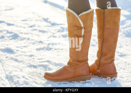 Leg woman winter brown fur boots walking on the snow in a winter park. Closeup outsole of warm boot. Stock Photo