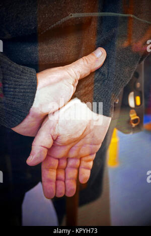 Man with hands clasped behind back against glass screen Stock Photo