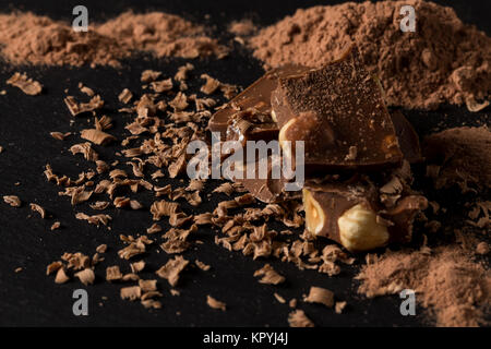 Broken chocolate nuts pieces and cocoa powder on dark background Stock Photo