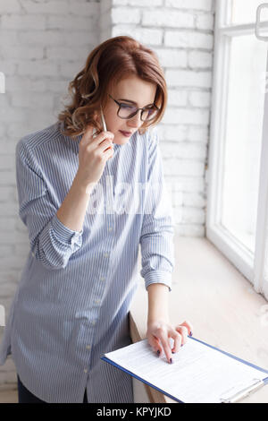 Young businesswoman consulting a document as she talks on the phone in the office, close up profile view Stock Photo