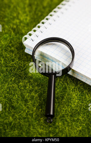 Notebook and magnifier on the grass close-up. Stock Photo