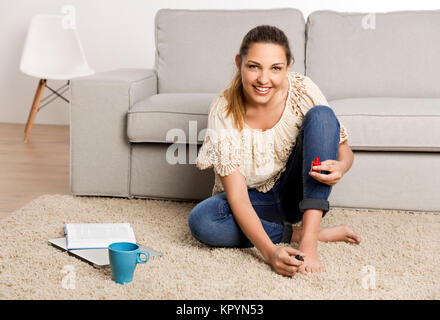 Beautiful happy woman at home making a pause to painting her nails Stock Photo