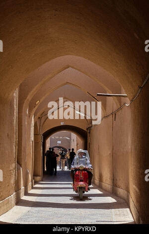Yazd, Iran - April 21, 2017: An elderly man rides a scooter through a covered street with clay arches. Stock Photo