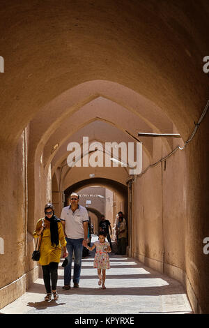 Yazd, Iran - April 21, 2017:  Pedestrians walk along a narrow covered arched lane with clay walls. Stock Photo