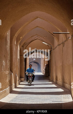 Yazd, Iran - April 21, 2017: An unknown young Iranian man is riding a moped along a narrow arched street. Stock Photo