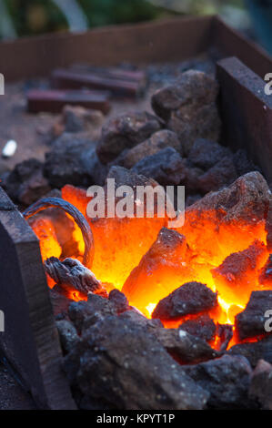 blacksmith furnace with burning coals, tools, and glowing hot metal workpieces, close-up Stock Photo
