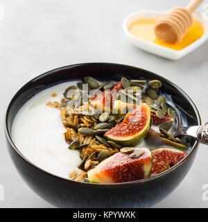 Healthy breakfast natural yogurt bowl with home made granola, pumpkin seeds and figs on gray background Stock Photo