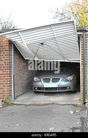One of a row of four garages for cars in road behind shops damage to up & over door BMW car inside unclear as to how damage occured Essex England UK Stock Photo