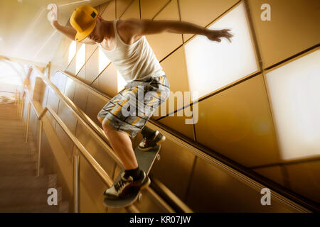 young skateboarder with basecap and shorts sliding down stairs in front of yellow background and back lighting Stock Photo