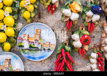 Hand painted plate with the Castello Scaligero in Sirmione, Italy, hanging on a wall with a set of pottery made fruits and vegetables Stock Photo