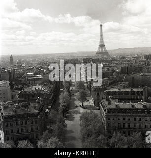 1950s, Paris, France, and a historical view from overhead of a long tree-lined boulevard with the famous wrought iron tower, the Eiffel Tower in the distance. One can see at this time how tall and defining the tower was compared to the other buildings in the city which were a uniform height. Stock Photo