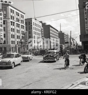 1950s, historical picture showing a bustling post-ww2 Toyko with cars, trucks and cyclists competing for space at a road junction without any traffic lights. Stock Photo