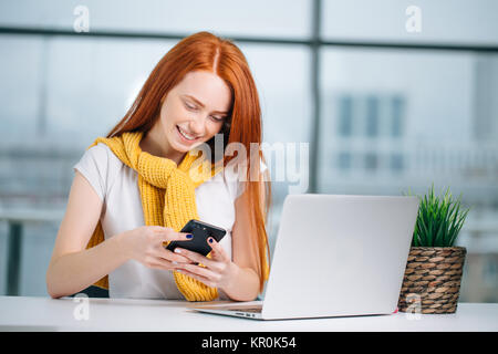 business woman sitting in office, looking at graphics and uses smartphone Stock Photo