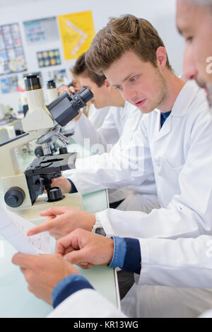 Students in lab using microscopes, reading paperwork Stock Photo