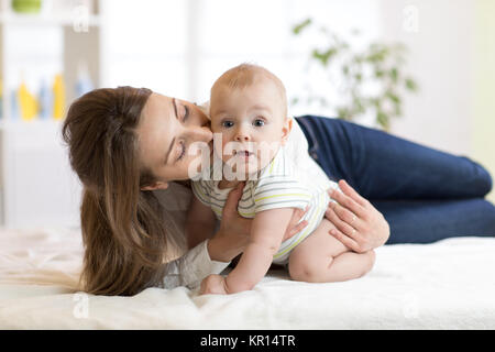 Mom kissing her little son on bed. Mother embracing infant baby. Stock Photo