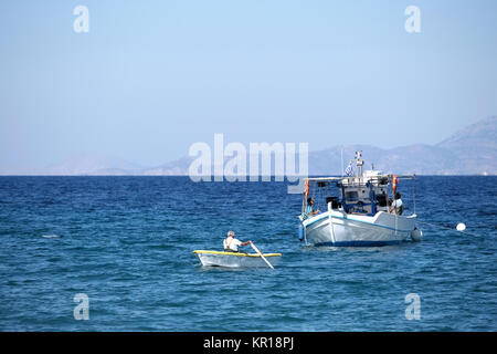 A local elderly fisherman rows to shore with a catch of freshly caught fry, small fish, to be sold immediately at a road side stall. Aegean sea Stock Photo