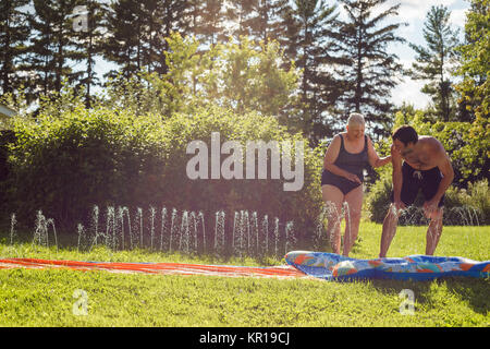 Man and his mother playing on a slip and slide in the garden Stock Photo