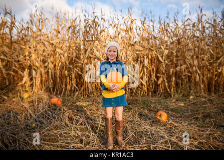 Girl standing in a pumpkin patch holding a pumpkin Stock Photo