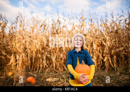 Girl standing in a pumpkin patch holding a pumpkin Stock Photo