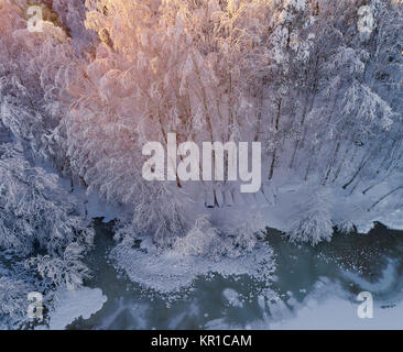 Aerial view of lake shore at winter after fresh snow with boats upside down on the shore and golden sunlight in Kurjenrahka National Park, Finland Stock Photo