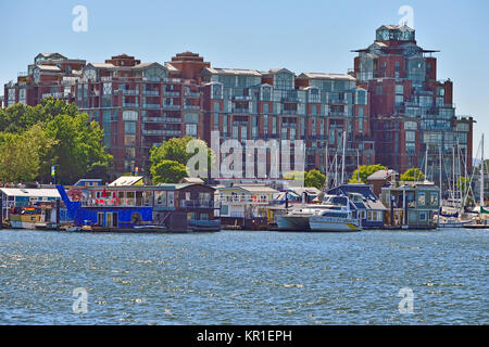 A group of floating homes thed up to a dock in front of a large condo complex at the Victoria harbour on Vancouver Island, British Columbia Canada. Stock Photo