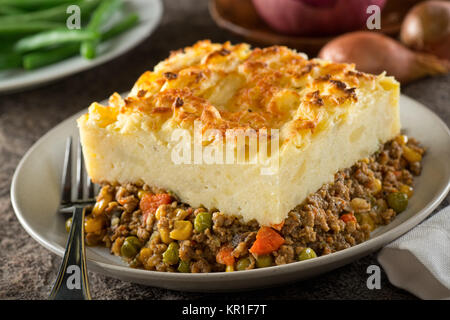 A serving of delicious homemade shepherd's pie with ground meat, mashed potato, carrots, peas, corn, and cheddar cheese crust. Stock Photo