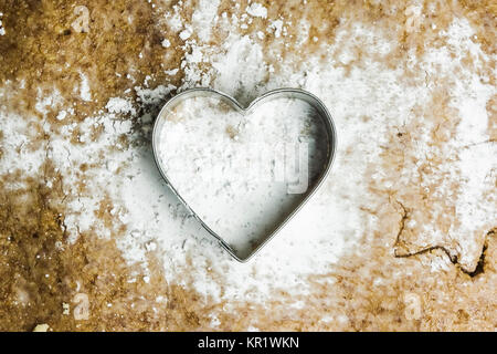 A heart shaped pastry cutter on a paste with icing sugar on it. The pastry cutter is used to make traditional christmas cookies. Love baking concept. Stock Photo