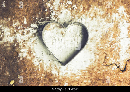 A heart shaped pastry cutter on a paste with icing sugar on it. The pastry cutter is used to make traditional christmas cookies. Love baking concept. Stock Photo